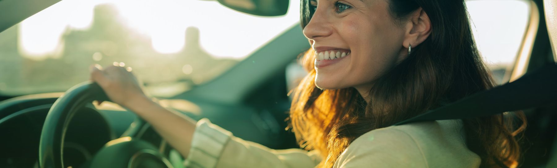 Eine junge Frau am Steuer ihres Autos, die Freiheit und Glück empfindet und während der goldenen Stunde mit einem strahlenden Lächeln zur Arbeit fährt