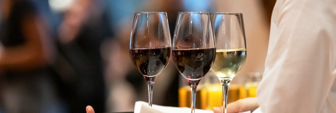 Kellner trägt ein Tablett mit zwei Rotwein- und einem Weißweinglas.