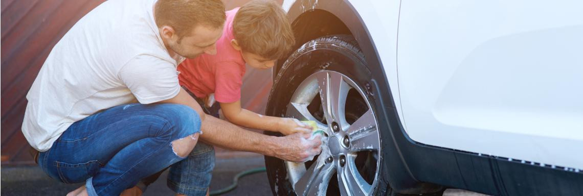 Mann und Kind waschen draußen vor der Garage ein Auto