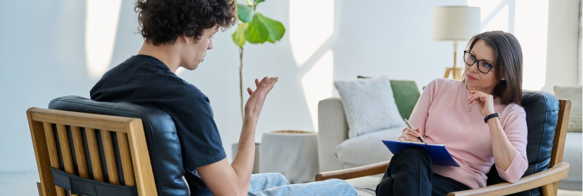 Psychotherapeutin und Patientin sitzen sich auf Stühlen gegenüber bei Therapiestunde