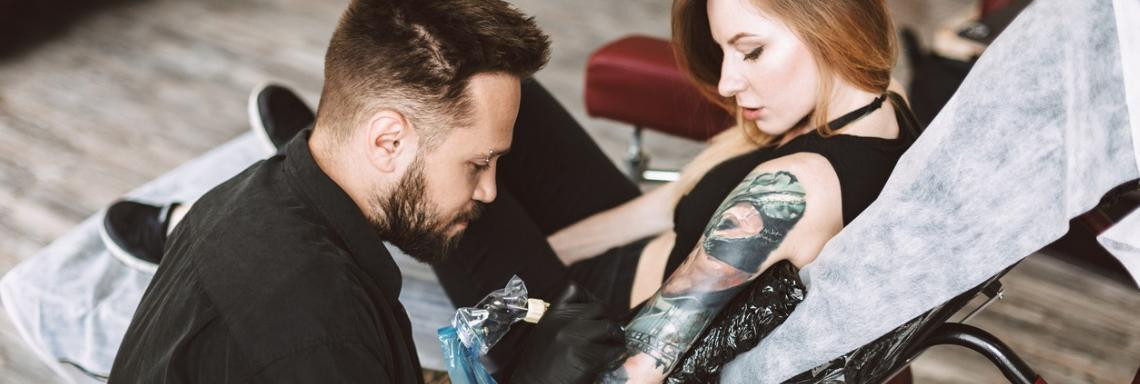 Tattoo Artist sticht Frau im Studio ein Tattoo auf dem Arm