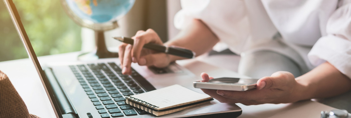 Person macht Urlaubsplanung mit Laptop, Smartphone und Notizblock