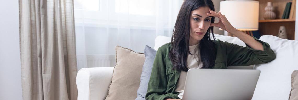 Junge dunkelhaarige Frau sitzt konzentriert mit Laptop auf dem Sofa 
