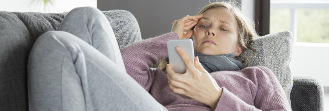 Kranke Frau mit Schal schreibt eine Nachricht am Handy.