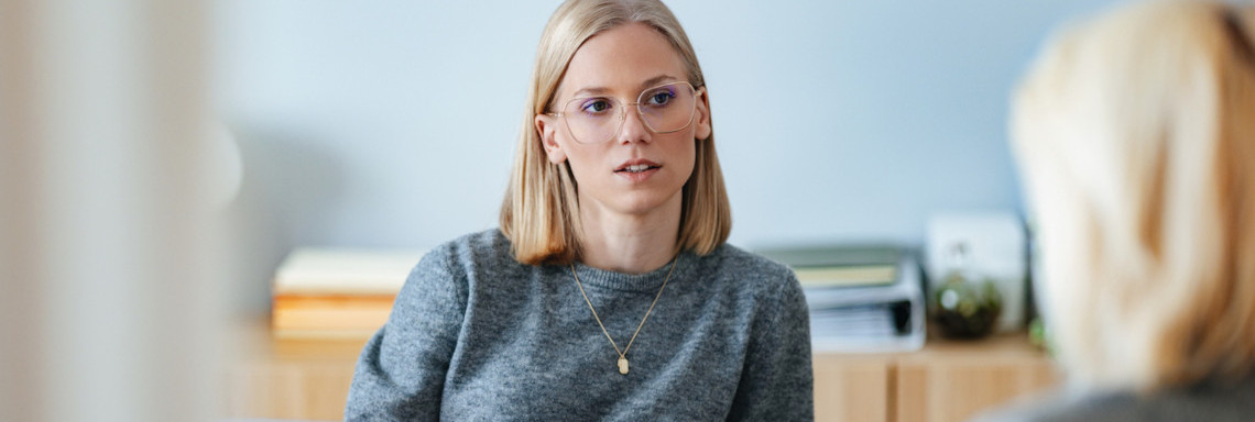 Junge blonde Frau sitzt bei einem Bewerbungsgespräch in einem Büro einer anderen Person gegenüber