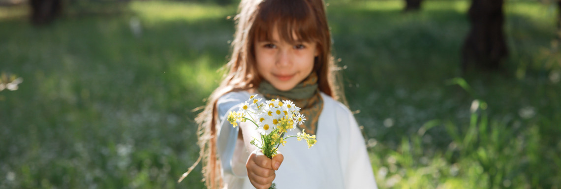 Mädchen steht bei Sonnenschein auf einer Wiese und hält einen Wildblumenstrauß in der Hand