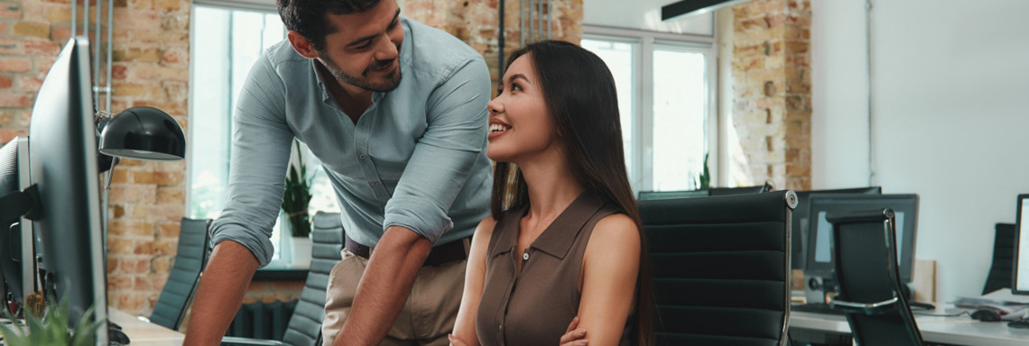 Happy to work with you! Two cheerful young colleagues in casual wear looking at each other with smile and discussing fresh ideas while working together in modern office. Workplace. Business concept.