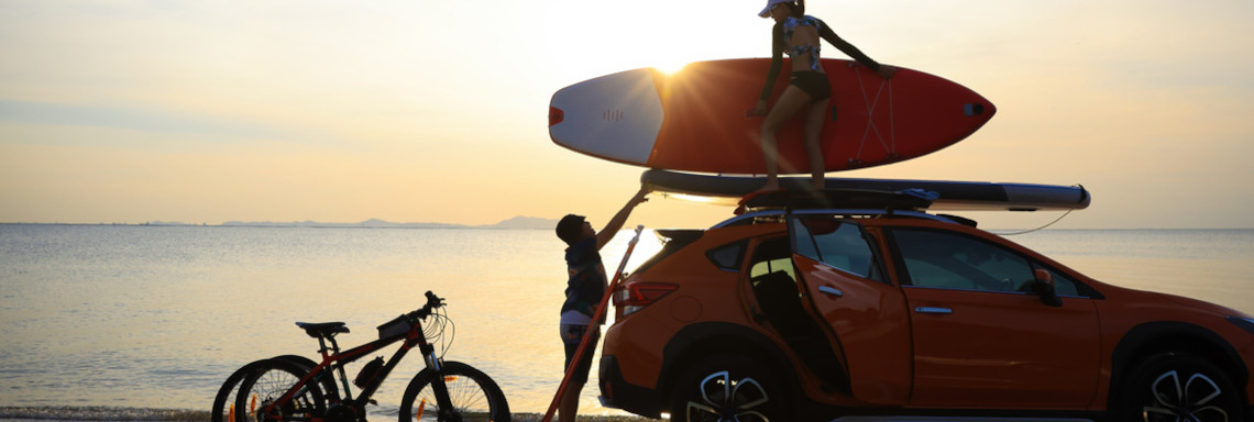 Silhouette couple traveler take paddle board to roof rack of car against sunset sky . Sport activity and lifestyle after workout at beach