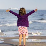 Kind steht mit ausgestreckten Armen am Strand 
