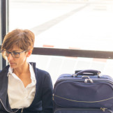 Zug zum Flug verpasst: Frau sitzt mit dem Handy in der Hand und dem Handgepäck neben sich am Flughafen