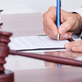Richter am Amtsgericht: er schreibt mit einem blauen Kugelschreiber, sein Richterhammer liegt auf dem Schreibtisch