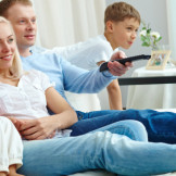 Junge Familien sitzt auf dem Sofa, Fernbedienung in der Hand