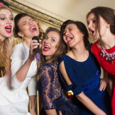 Gruppe junger Frauen in Abendgarderobe singt inbrünstig in ein Mikrophon