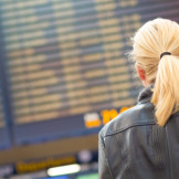 Blonde Touristin steht bei Flugbegleiter-Streik vor der Anzeigetafel am Flughafen
