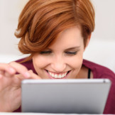 junge Frau tippt auf dem iPad und freut sich übers Verkaufen bei eBay