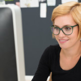 Ergonomie am Arbeitsplatz: junge Frau mit Brille und kurzen Haaren sitzt vor dem Computer-Bildschirm