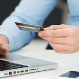 Phishing: Ein Mann sitzt vor einem Laptop und hält eine Kreditkarte in der Hand.