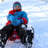 Schlitten und Snowboard fahren: Ein Kind sitzt auf einem Schlitten: