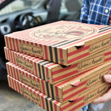 Urteil: Stundenlohn von 3,40 Euro ist sittenwidrig. Ein Mann in einem blauen Karohemd hält vier Pizzaschachteln.