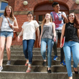 Hitzefrei in der Schule: So unterschiedlich ist es geregelt. Jugendliche gehen eine Steintreppe vor einem roten Backsteingebäude hinab.