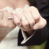 Behördengänge nach der Hochzeit: die Checkliste. Ein Brautpaar das seine kleinen Finger der rechten Hand verschlungen hält.