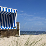 Erholungskur: Keine Entgeltfortzahlung für Arbeitnehmer. EIn blau-weiß gestreifter Strandkorb steht in den Dünen, dahinter sieht man das Meer.
