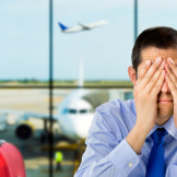 Fluggastrechte durchsetzen: Neue Leitlinien auf EU-Ebene. Ein Mann sitzt im Flughafen-Terminal und hält sich beide Hände vors Gesicht.