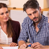 Ehegattensplitting: Wann gilt die Zusammenveranlagung? Ein junges Paar sitzt mit einem Mann an einem Tisch.