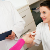 Elektronische Gesundheitskarte ist verpflichtend. Eine Patientin reicht einer Arzthelferin eine Chipkarte.