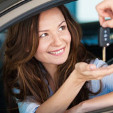 Privates Carsharing: Auto teilen ohne Risiko. Eine Frau sitzt im Auto und hält die Hand auf. Eine andere Person legt einen Autoschlüssel hinein.