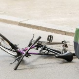 Radweg falsch benutzt: Radfahrer hat Mitschuld an Unfall. Vor einem grünen Auto liegen ein umgestürztes Fahrrad und ein Fahrradhelm.
