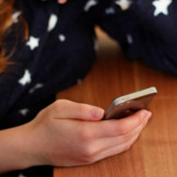 WhatsApp-Datenschutz: Weitergabe an Facebook rechtens? Ein Mädchen mit roten Haaren und schwarzem Pullover mit weißen Sternen hält ein Smartphone in der Hand.