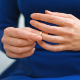 Trennungsjahr vor der Scheidung: So läuft es ab. Eine Frau in blauem Kleid zieht einen goldenen Ring über den Ringfinger.