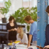 Arbeitsstättenverordnung 2016: Das sind die Neuerungen. In einem offenen Büro steht ein Mann, der auf ein Tablet schaut. Im Hintergrund stehen mehrere Personen an einem Schreibtisch.