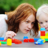 Au-pair aufnehmen: Was die Gastfamilie wissen sollte. Eine junge Frau schaut gemeinsam mit einem Kleinkind auf eine Plastik-Eisenbahn.