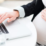 Mutterschutzgesetz: Neue Regelungen ab 2017. Ein schwangere Frau sitzt an einem Notebook und hält sich mit einer Hand den Babybauch.