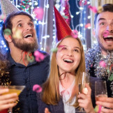 Nachtruhe an Silvester: Das sind die Regeln. Vier junge Männer und Frauen sind feierlich gekleidet. Konfetti regnet auf sie herab.