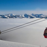 Schneegarantie: Welche Rechte haben Winterurlauber? Die Gondel einer Seilbahn schwebt über Wolken verhangenen Bergen.