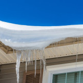 Dachlawine: Haftet der Hausbesitzer für Schäden? An einer Dachkante hängen Schnee und Eiszapfen herunter.