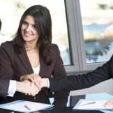 Schlichtungsverfahren: Informationspflicht für Unternehmen. Drei Personen im Business-Outfit sitzen an einem Tisch. Der Mann und eine der Frauen reichen sich die Hände.