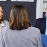 Im Büro: Zwei Frauen sprechen mit einem Mann, der eine blaue Mappe in der Hand hält