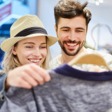 Junges glückliches Paar freut sich beim Shopping über Kleidung im Modeladen
