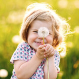 glückliches Kind mit Pusteblume auf einer Wiese im Sonnenschein