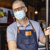 Gastronom mit Maske auf, öffnet seine Restaurant Tür