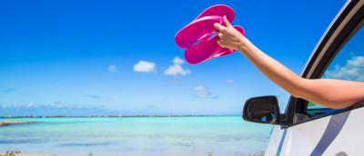 Barfuß Auto fahren: Frau hält Flip Flops aus dem Autofenster Barfuß Auto fahren: Frau hält Flip Flops aus dem Autofenster