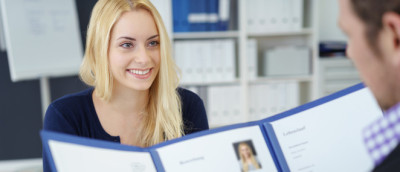 Rechtliches zum Praktikum: Mindestlohn und Dauer. Eine blonde junge Frau sitzt einem Mann gegenüber, der sich ihre Bewerbungsmappe ansieht. Rechtliches zum Praktikum: Mindestlohn und Dauer. Eine blonde junge Frau sitzt einem Mann gegenüber, der sich ihre Bewerbungsmappe ansieht.