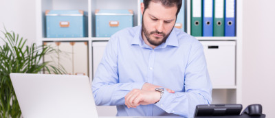 Arbeitszeitbetrug: Wann Abmahnung oder Kündigung drohen. Ein Mann in hellblauem Hemd sitzt an einem Schriebtisch im Büro und guckt auf seine Armbanduhr. Arbeitszeitbetrug: Wann Abmahnung oder Kündigung drohen. Ein Mann in hellblauem Hemd sitzt an einem Schriebtisch im Büro und guckt auf seine Armbanduhr.