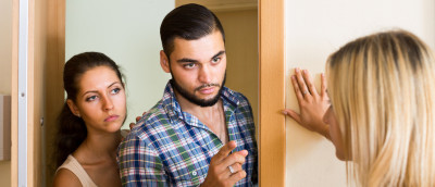 Hausverbot erteilen: Das erlaubt das Hausrecht. Ein junges Paar steht in der Wohnungstür einer anderen Frau gegenüber. Der Mann hebt seinen Finger. Hausverbot erteilen: Das erlaubt das Hausrecht. Ein junges Paar steht in der Wohnungstür einer anderen Frau gegenüber. Der Mann hebt seinen Finger.