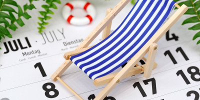 Nahaufnahme kleiner Spielzeug-Liegestuhl und -Schwimmring stehen auf Kalender