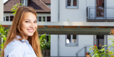 Lächelnde, junge Mietern steht vor einem Mehrfamilienhaus